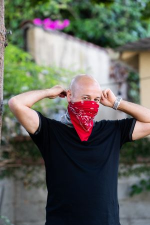 Man tying red bandana around his nose and mouth for protection against COVID