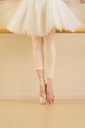 Ballet dancer at barre with one foot in pointe shoes