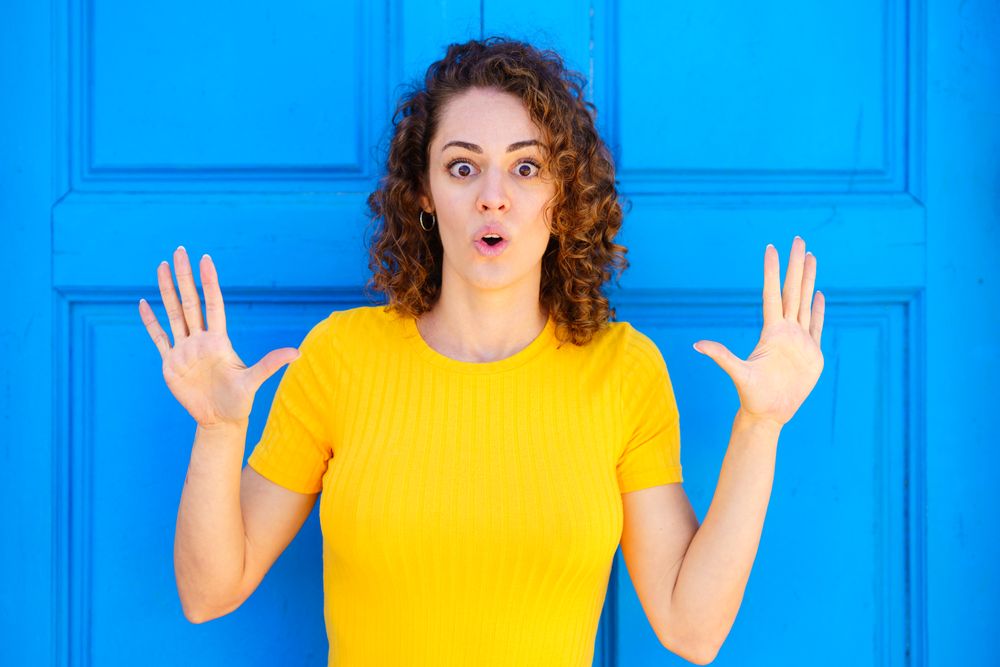 Surprised woman in yellow dress against a closed blue door