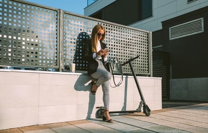 Businesswoman using mobile with her scooter next