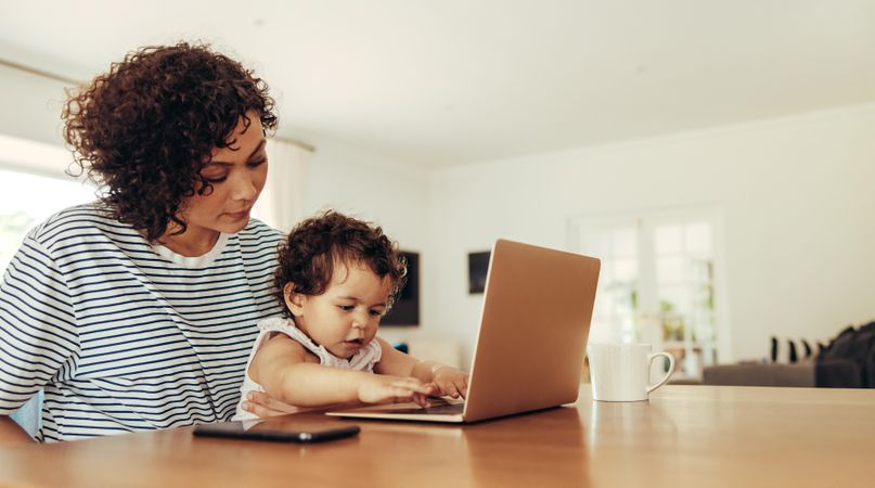 Mother holding her baby while she explores laptop computer