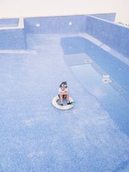 Kid with lifebuoy sitting in empty pool