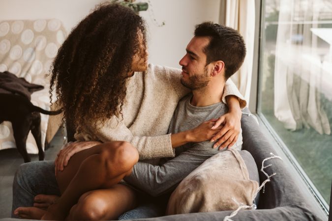 Young multiracial couple hugging on sofa