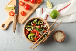 Fresh salad with chopsticks and kitchen accessories on grey background, top view