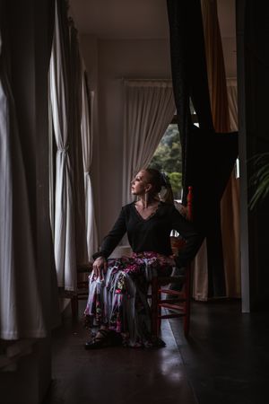 Woman dancer in suit for flamenco sitting and looking out window