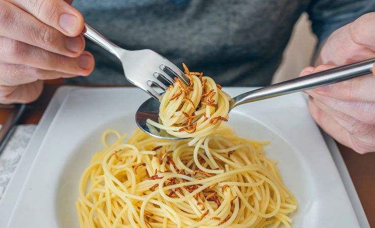 Hands of man eating spaghetti with worms