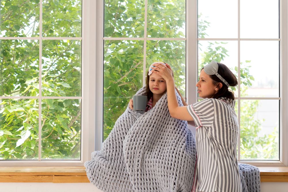 Mother caring for sick daughter at home near window.