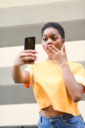 Female taking photo with mouth covered in front of striped wall, vertical composition