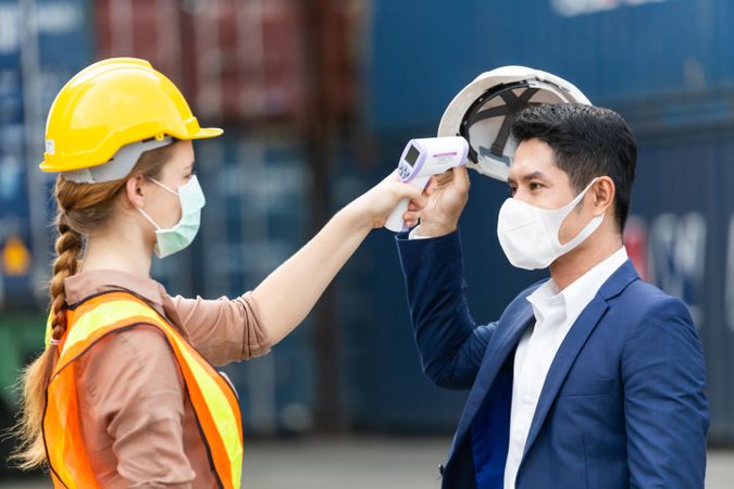 Man removing hard hat for woman to take his temperature