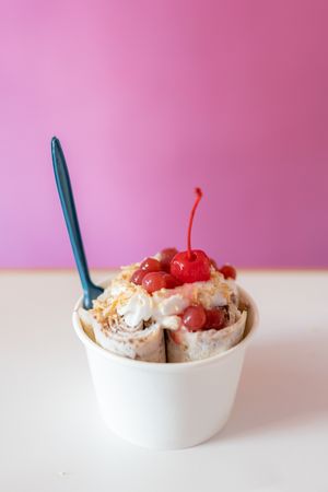 Close up of a rolled ice cream decorated with strawberry bubbles, nut toppings and a cherry on top