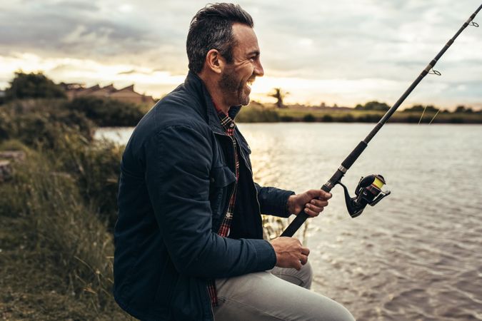 Smiling man sitting beside a lake and fishing