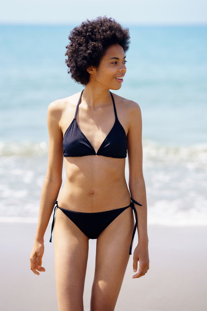 Smiling woman walking on shore in bikini looking around