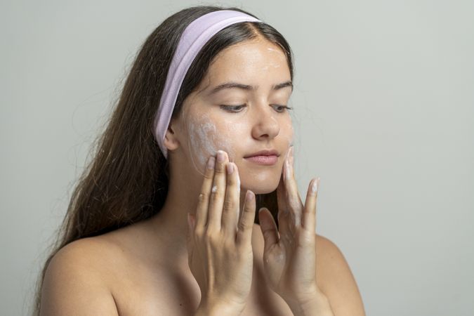 Young woman applying facial scrub cream on natural skin texture in bright home studio