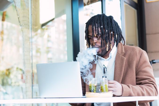 Smoking Black man using laptop on restaurant terrace