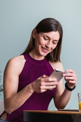 Cheerful adult female browsing mobile phone in house on blurred background