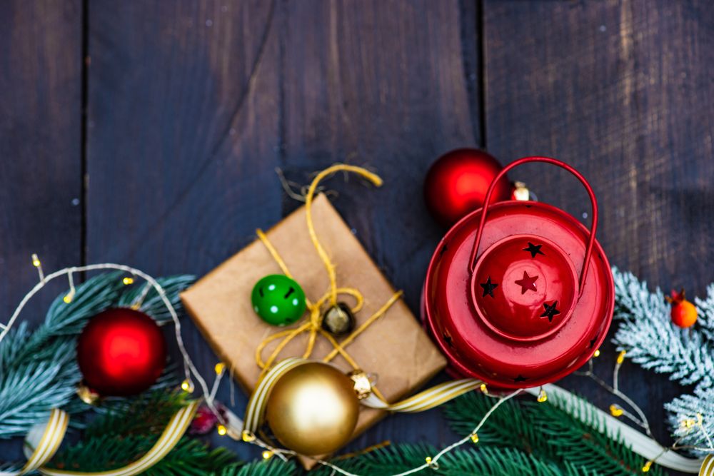 Top view of Christmas gift wrapped in brown paper surrounded by baubles with light string