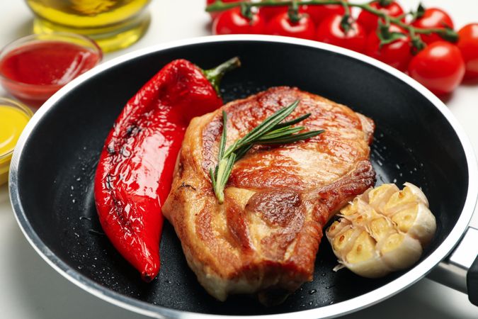 Pan with fried steaks and ingredients for cooking on blank background, close up