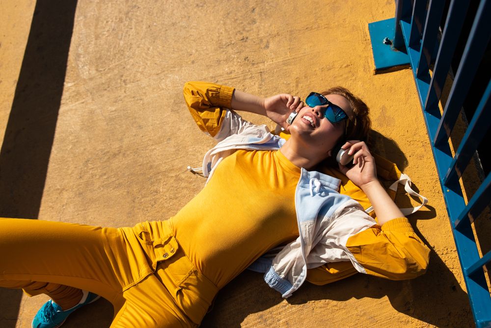 Stylish young woman in vibrant clothes enjoying music on street