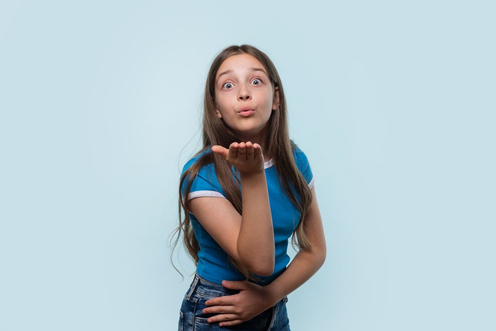 Girl in blue shirt blows a kiss towards the camera