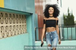 Young woman with afro hair strolling next to a modern colorful building bDkjK4