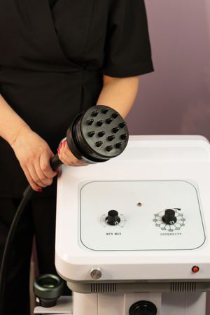 Beautician holding cavitation handpiece near machine control unit.
