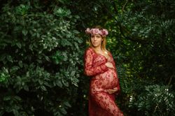 Pregnant woman with closed eyes touching belly and chin while standing in garden in sunny day