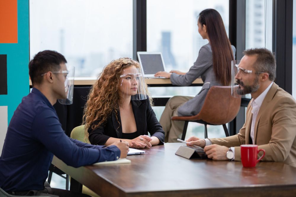Male manager in face shield explaining work project to colleagues in the office