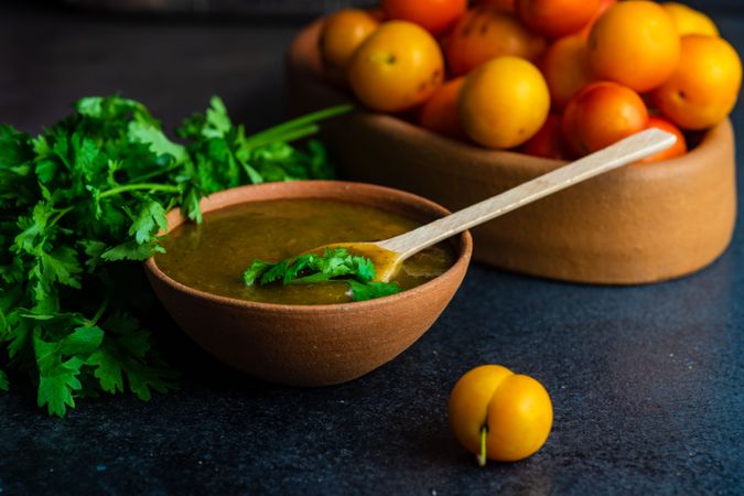 Bowl of plums and fresh parsley with Georgian Tkemali Sauce on dark counter