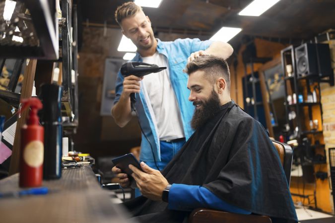 Man checking his phone while having his hair styled in a salon