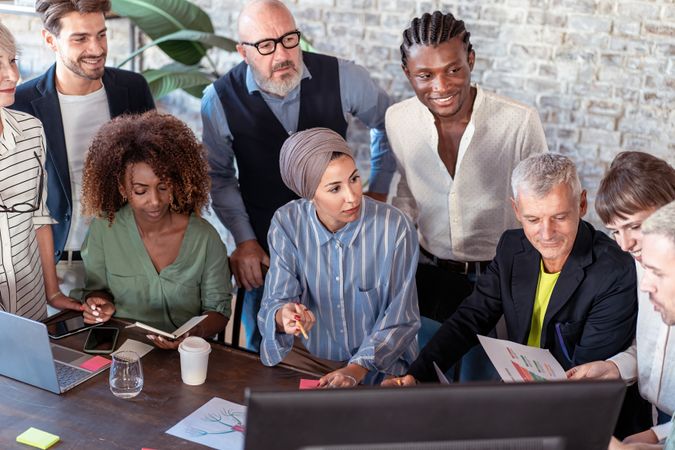 Diverse group of professionals brainstorming around a laptop in a modern workspace