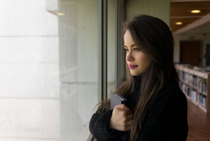 Woman with book looking out window