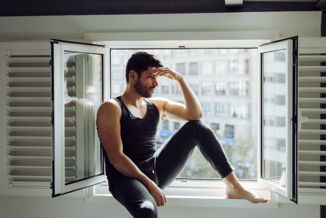 Young pensive man sitting on window
