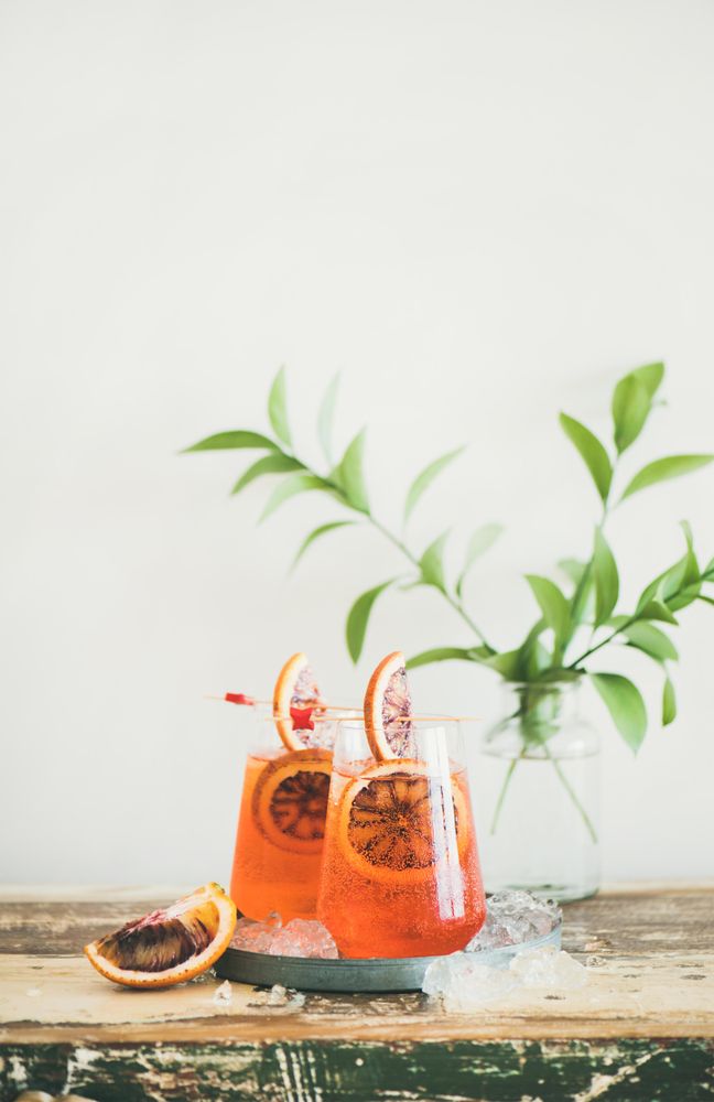 Two glasses of an orange cocktail with orange slices, and leaves in background, with copy space
