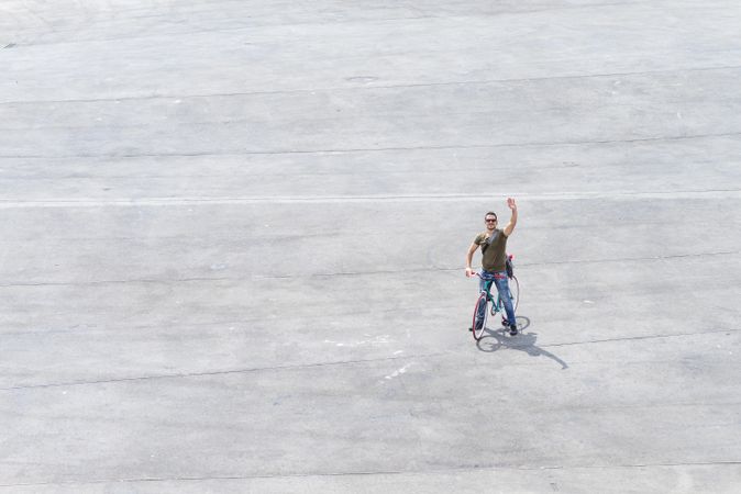 Male standing on bike and waving on cement with space for text