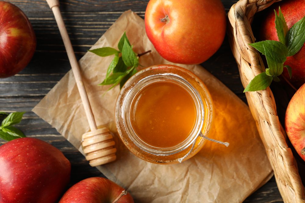 Looking down at pot of honey with dipper and apples