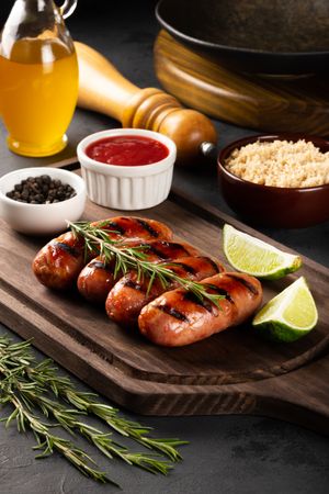 Grilled sausages on board with condiments, sides and lime slices, vertical