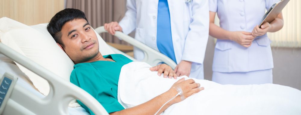 Male patient in hospital bed looking at camera with doctor and nurse at bedside