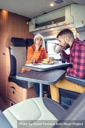 Male and female friend enjoying breakfast rolls and coffee in back of van, vertical 5rQ8M0