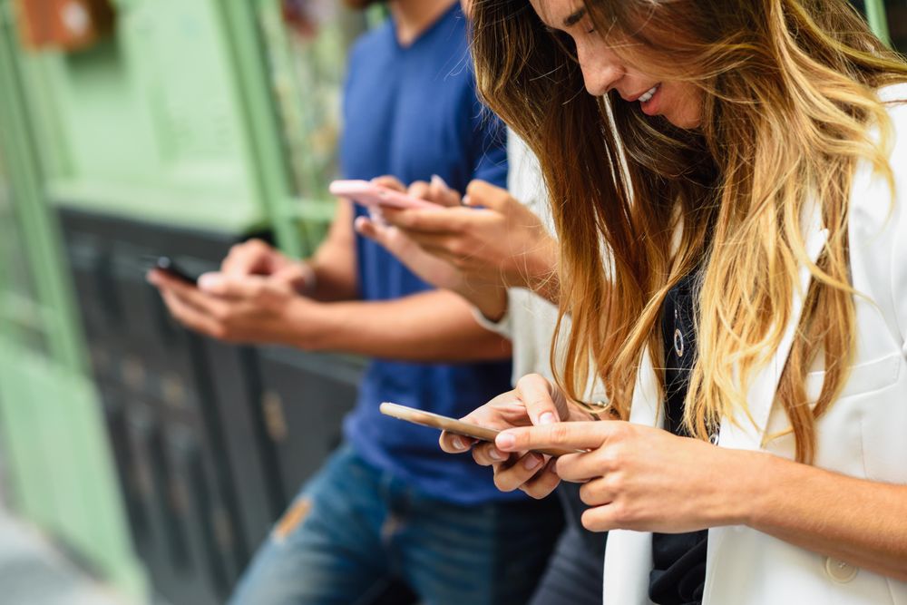 Friends checking their phones by green wall