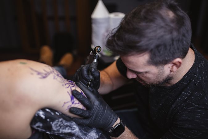 Master doing tattoo on forearm of male customer