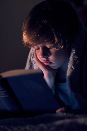 Cute boy reading boy in dark room