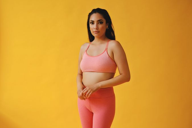 Hispanic woman in yoga clothes standing in yellow studio, copy space
