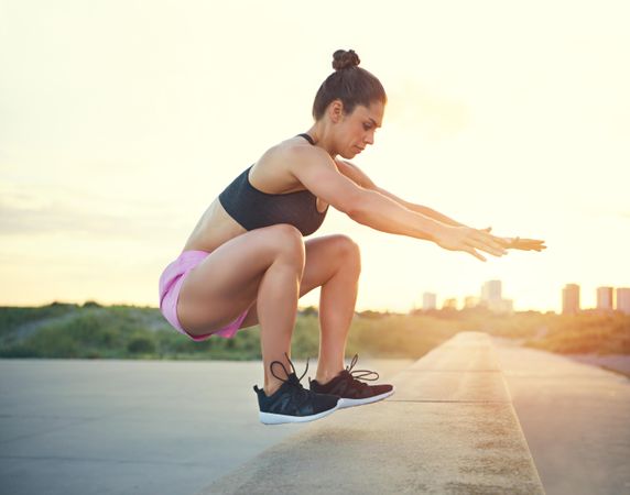 Muscular woman jumping up onto wall during morning workout