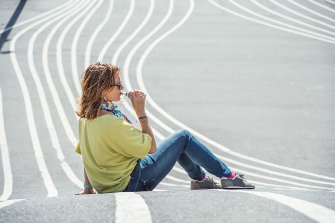 Modern relaxed woman vaping while sitting on marked road