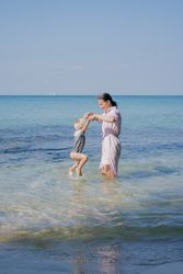 Woman and small kid having fun with water while relaxing on seacoast at resort