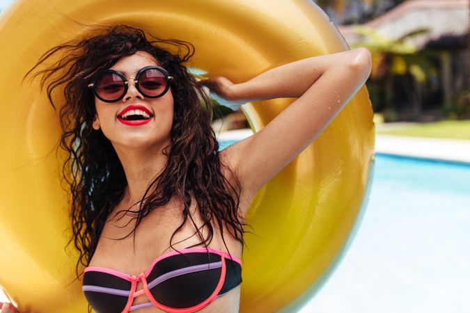 Portrait of woman in bikini posing with inflatable ring near swimming pool