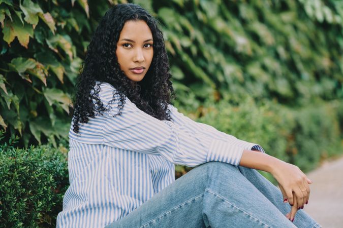 An Elegant Woman Posing Gracefully in a Striped Shirt Surrounded by Lush Greenery