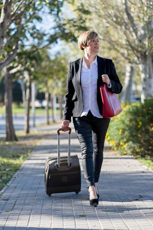 Confident businesswoman walking outside on sunny day with suit case in hand