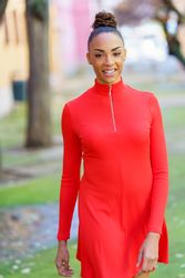 Smiling female in casual red dress strolling outside, vertical composition