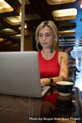 Tattooed young woman working on laptop computer in a coffee shop bDmYV0